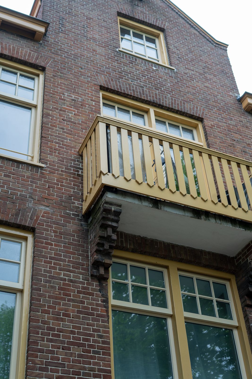 Detail van een houten balkon met okergeel schilderwerk